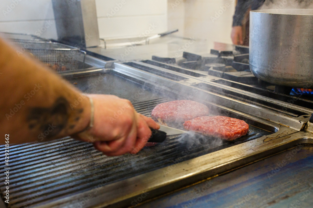 Hamburger di carne in cottura su una piastra rovente di un pub