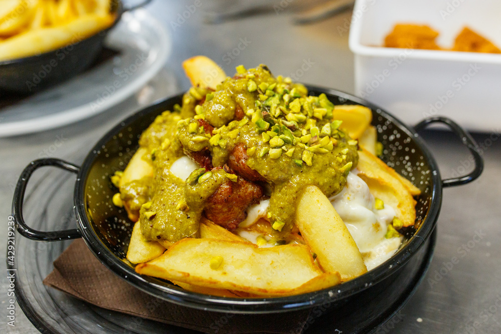 Foto Stock Porzione di patatine fritte con pesto di pistacchio, polpettine  fritte, formaggio fuso e granella di pistacchio | Adobe Stock