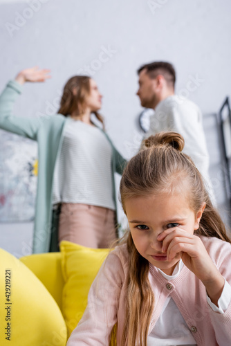 Crying kid sitting near blurred parents quarrelling.