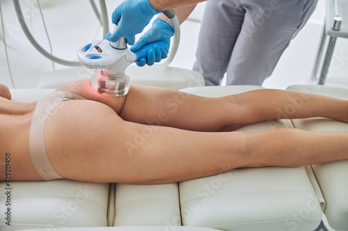 Focused image of beautician doing Rf skin tightening in body client in beauty center