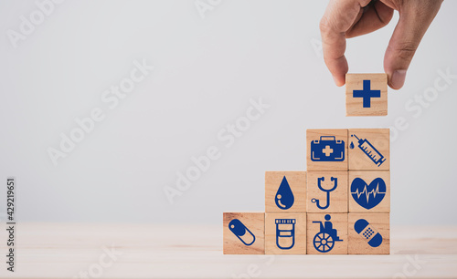 Hand holding wooden stacking with healthcare medical and hospital icons on table , Health and insurance concept.