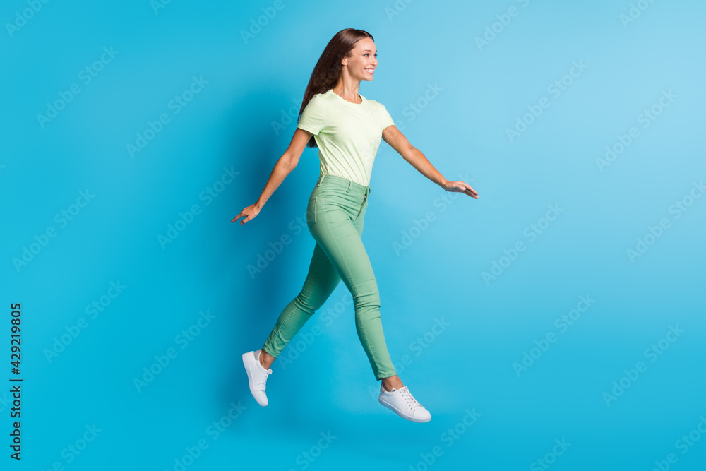 Full size profile photo of optimistic brunette lady jump go wear t-shirt trousers sneakers isolated on blue color background