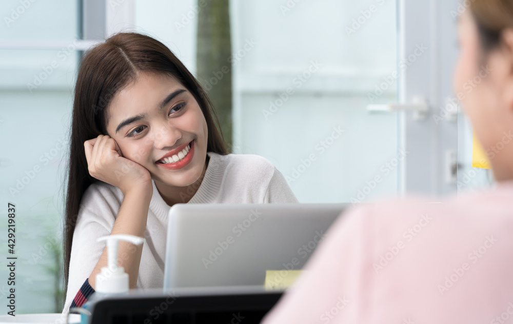 Female colleagues are talking, consulting or gossiping at the Home Office. Two young women sitting at the opposite desk chatted and smiled happily during the break in bussiness concept,Soft focus. Female colleagues are talking, consulting or gossiping at the Home Office. Two young women sitting at the opposite desk chatted and smiled happily during the break in bussiness concept,Soft focus.