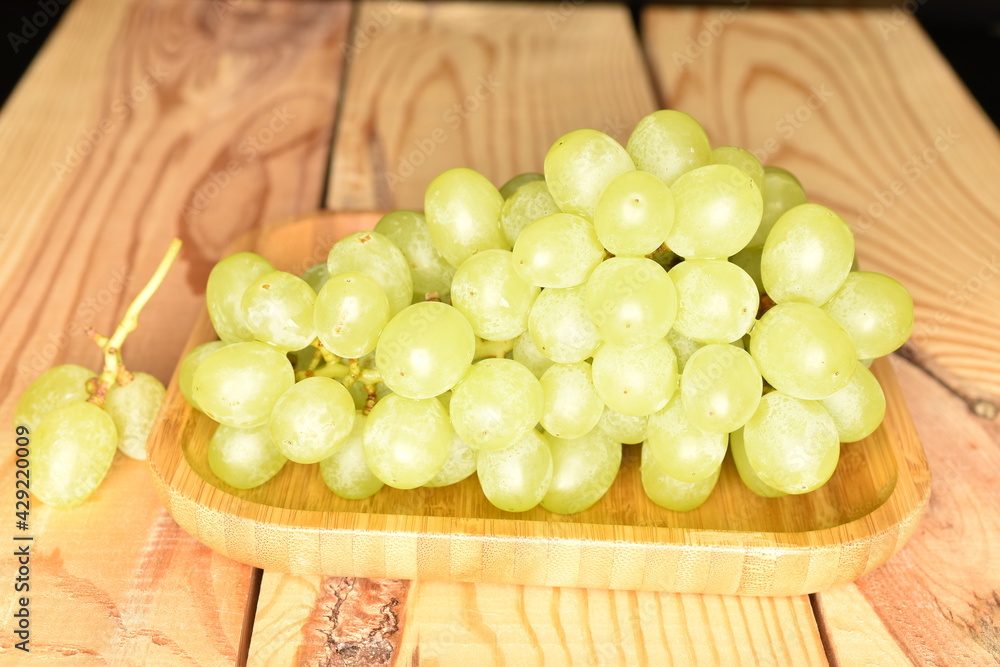 Ripe bunch of sweet grapes in a bamboo plate on a wooden table, close-up. Ripe bunch of sweet grapes in a bamboo plate on a wooden table, close-up.