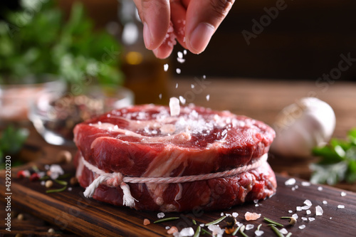Fényképezés Hand sprinkling salt on fresh raw beef meat on a cutting board