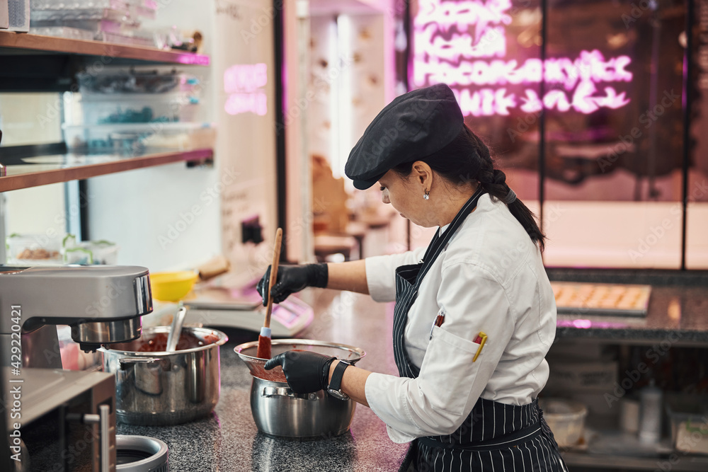 Fototapeta premium Concentrated female cook using wooden spatula for stirring