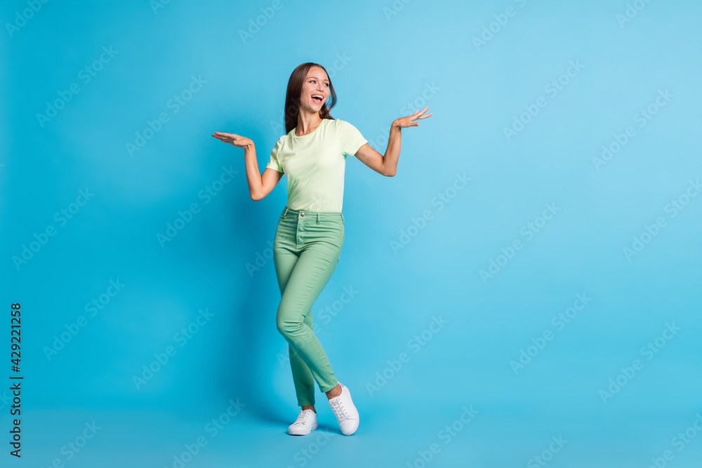 Obraz premium Full size photo of impressed brunette lady dance look empty space wear t-shirt trousers sneakers isolated on blue background
