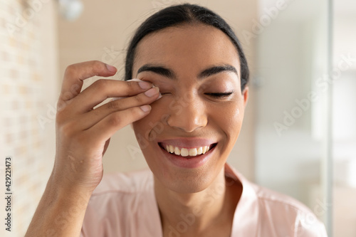 Portrait of smiling mixed race transgender woman reflected in bathroom mirror removing eye makeup photo