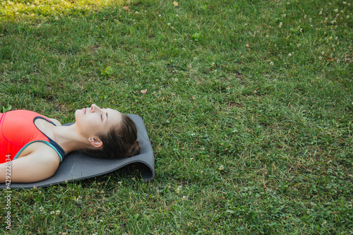 European girl in a light tracksuit doing yoga in the park in the afternoon in the summer. Gymnastics in nature. Thin woman outdoor