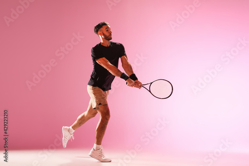 Young caucasian man playing tennis isolated on pink studio background, action and motion concept