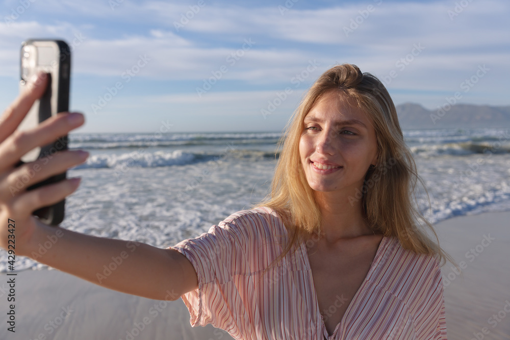 Caucasian woman wearing beach cover up taking a selfie with smartphone at the beach Caucasian woman wearing beach cover up taking a selfie with smartphone at the beach