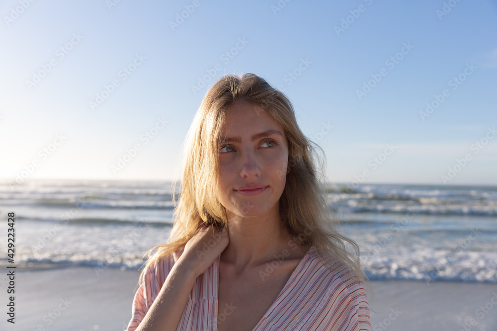 Caucasian woman wearing beach cover up touching her shoulder at the beach Caucasian woman wearing beach cover up touching her shoulder at the beach