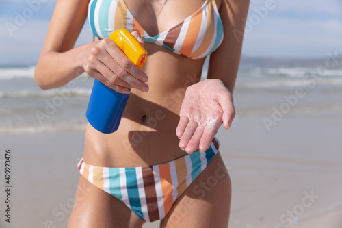 Caucasian woman wearing bikini putting sunscreen on at the beach