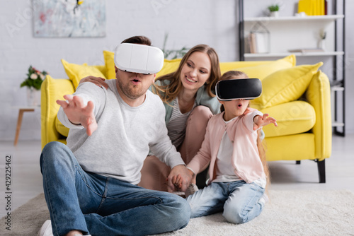 Excited man and daughter using vr headsets near mother at home.