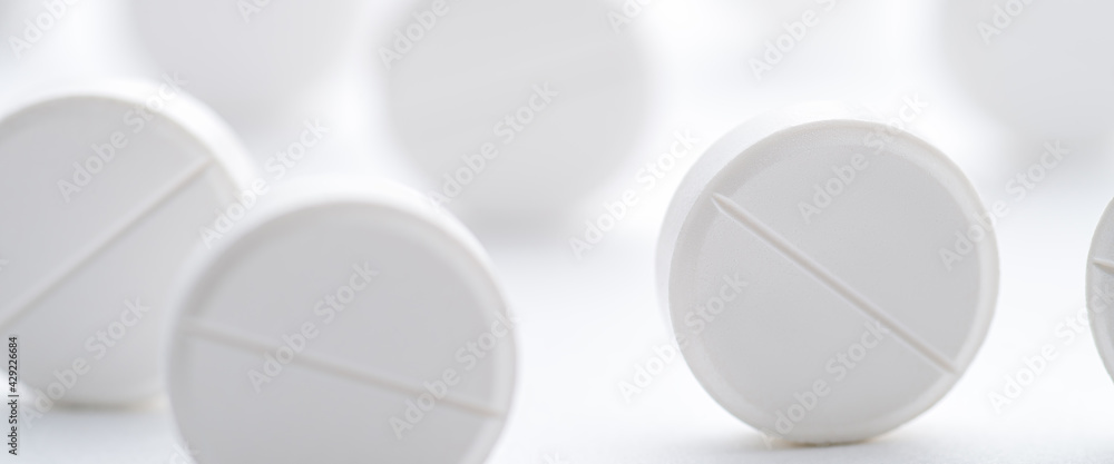 A pile of white pills scattered on a bright white background. Selective focus. A pile of white pills scattered on a bright white background. Selective focus.