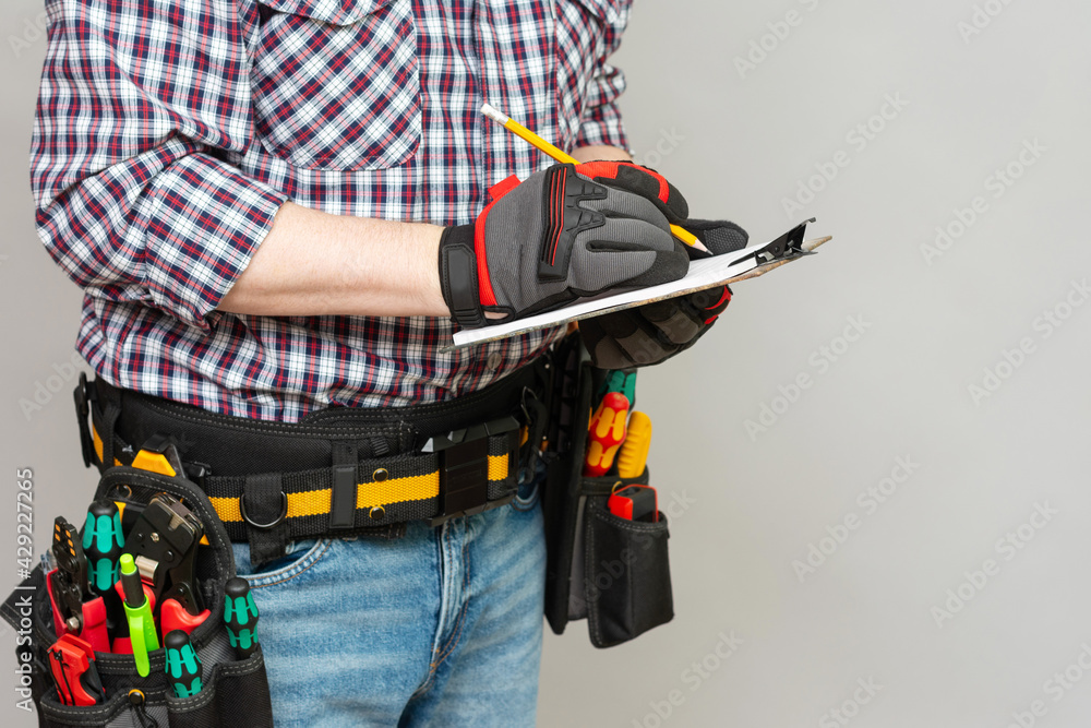 Builder worker or electrician holds a sheet of paper and a pencil in his hand. The concept of concluding a contract for the performance of installation works. Preparation of an estimate for constructi Builder worker or electrician holds a sheet of paper and a pencil in his hand. The concept of concluding a contract for the performance of installation works. Preparation of an estimate for constructi