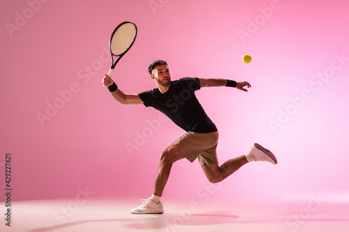 Fototapeta Naklejka Na Ścianę i Meble -  Young caucasian man playing tennis isolated on pink studio background, action and motion concept
