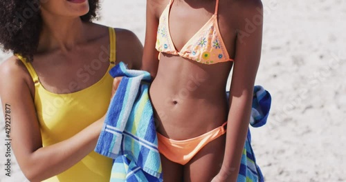 Smiling african american mother drying her daughter with a towel at the beach