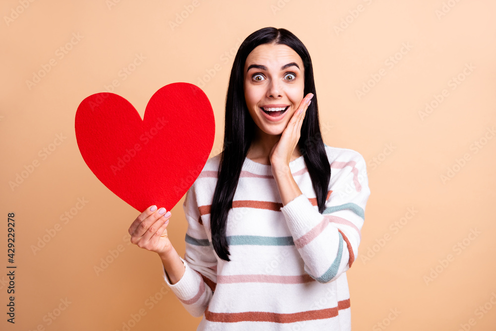 Photo of young girl happy smile amazed shocked surprised hold big red heart romantic isolated over beige color background Photo of young girl happy smile amazed shocked surprised hold big red heart romantic isolated over beige color background