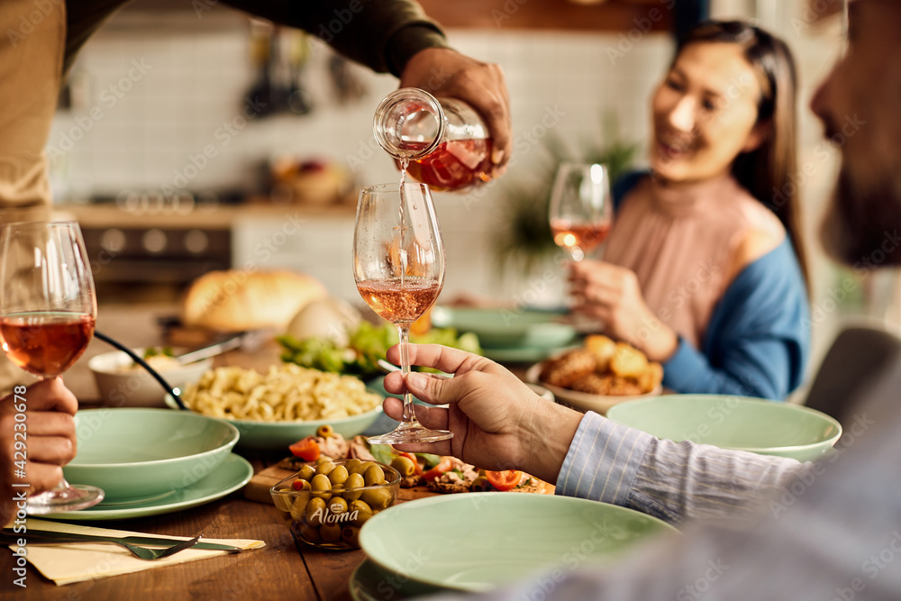 Close-up of man serving wine to his friends during lunch at home.