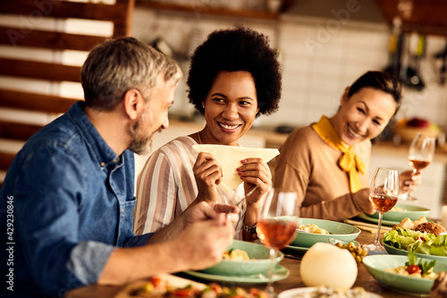Happy Black woman enjoying in conversation with her friends during a meal at dining table.