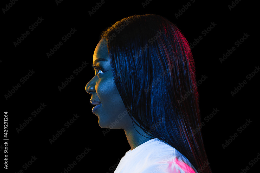 Fototapeta premium African young woman's portrait on dark studio background in neon. Concept of human emotions, facial expression, youth, sales, ad.