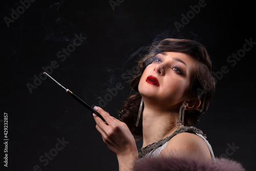 Retro woman portrait. A beautiful woman in the style of the 20s and 30s with a cigarette holder smokes.