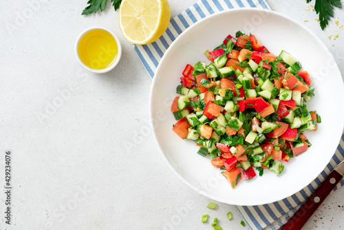 Vegetable salad on a white plate on a light background. Salad with tomatoes, cucumbers, peppers, parsley and lemon. Vegan or diet food. Copy space for text.