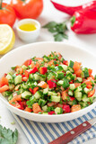 Vegetable salad in a white plate on a light background. Salad with tomatoes, cucumbers, peppers, parsley and lemon. Vegan or diet food.