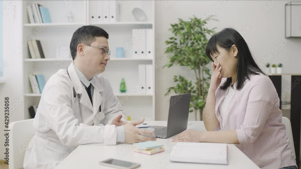 Oncologist delivering bad diagnosis to upset asian woman, supporting patient Oncologist delivering bad diagnosis to upset asian woman, supporting patient