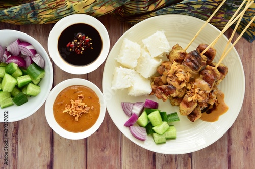 Indonesian chicken satay or Sate Ayam  with lontong. Served with sweet soy sauce, peanut sauce and pickles cucumber and onion