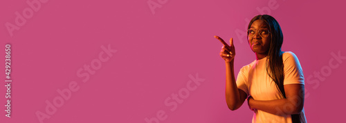 African young woman's portrait on pink studio background in neon. Concept of human emotions, facial expression, youth, sales, ad.