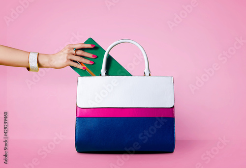 Handbag purse and beautiful woman hand with red manicure isolated on pink background