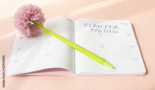 Photos Notebook on a pink background with a pen in the form of a flower and the inscription - plan for the spring