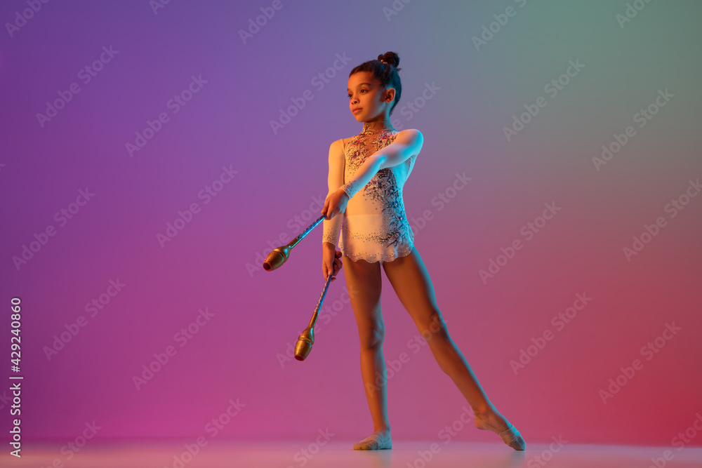 African-american rhythmic gymnast, pretty girl practicing on gradient studio background in neon light African-american rhythmic gymnast, pretty girl practicing on gradient studio background in neon light