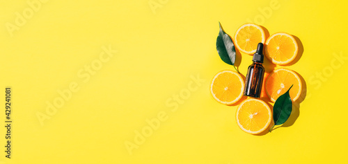 A bottle of cosmetic product oil serum gel made from a juicy ripe orange on a bright yellow background