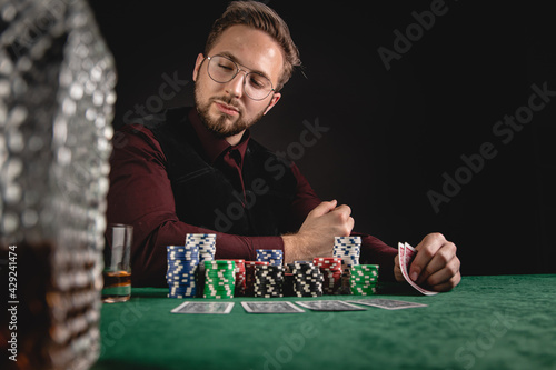 Young gentleman playing poker with whisky on green table 
