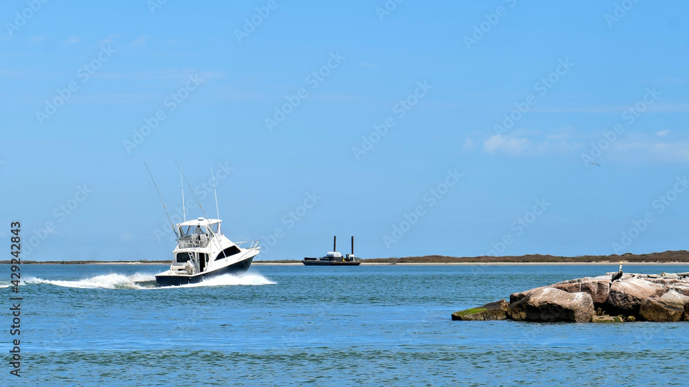 Broadside view of a beautiful white and black fishing yacht boat sails past rock breakwater on the calm blue water on a sunny day.