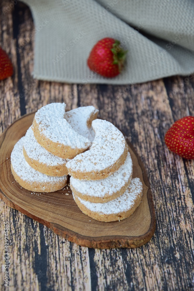 Putri Salju or crescent-shaped cookies coated with powdered sugar. Traditional Indonesian cookies to celebrate Eid al Fitr. Decorated with strawberries on wooden background
