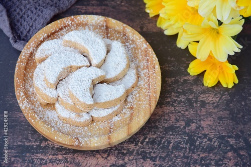 Putri Salju or crescent-shaped cookies coated with powdered sugar. Traditional Indonesian cookies to celebrate Eid al Fitr. Decorated with yellow flower on wooden background photo