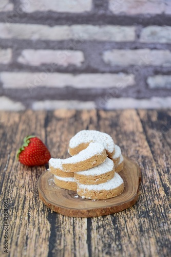 Putri Salju or crescent-shaped cookies coated with powdered sugar. Traditional Indonesian cookies to celebrate Eid al Fitr. Decorated with strawberries on wooden background photo