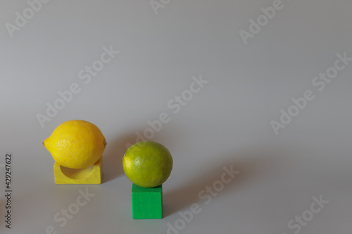 Abstraction with yellow lemon and green lime and wooden figure and cube on grey background.