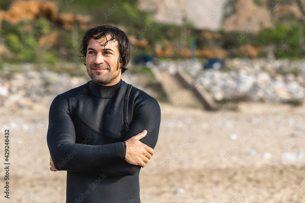 Medium shot young wet man wearing diving suit standing on the beach looking ahead with smiley face Medium shot young wet man wearing diving suit standing on the beach looking ahead with smiley face