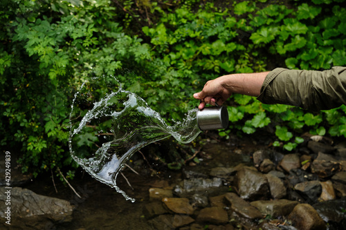 A splash of fresh water from a mug in the hands of a man on the background of nature. Drinking water concept. A splash of freshness. Natural water. Healthy lifestyle. cold water from a mountain river