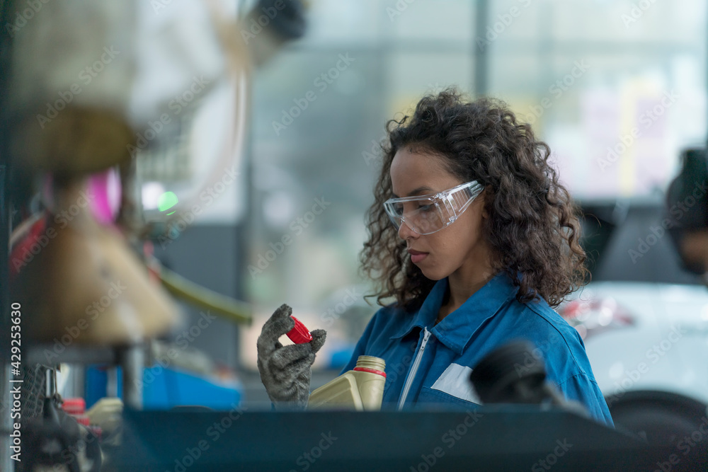 A female car mechanic holding a bottle of brake fluid and engine oil to be exchanged for a customer. Auto mechanic female automotive diagnostic Checking car service, repair, maintenance. A female car mechanic holding a bottle of brake fluid and engine oil to be exchanged for a customer. Auto mechanic female automotive diagnostic Checking car service, repair, maintenance.