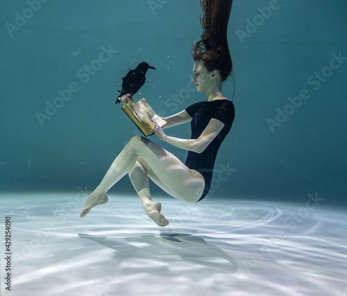 beautiful girl in a red swimsuit reads an interesting book underwater on a blue background 