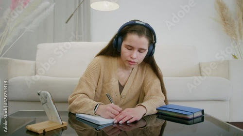 Student sitting at home wears headphones speaks with teacher online by laptop web camera write notes, studies on e-learning. photo