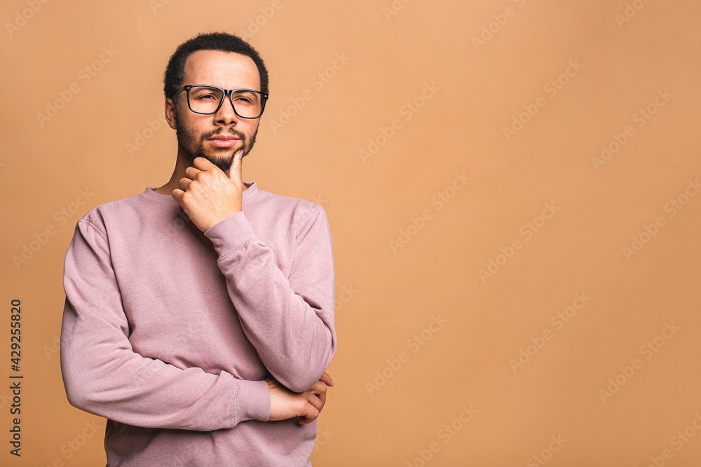 Fototapeta premium Thinking black Afro American man with serious expression looking, posing isolated against beige background.