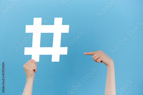 Horizontal images of female hands holding large big white hashtag sign, viral web content, internet promotion, isolated over blue studio background. Blogging blog website strategy concept