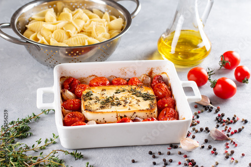 Feta cheese pasta sauce recipe step. Tomatoes drizzled with olive oil in a baking dish with a feta cheese block in the middle and sprinkled with salt and freshly ground pepper. photo